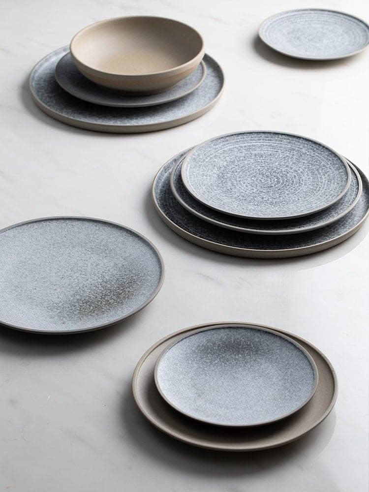 Grey speckled stoneware plates with a neutral bowl on a marble surface.